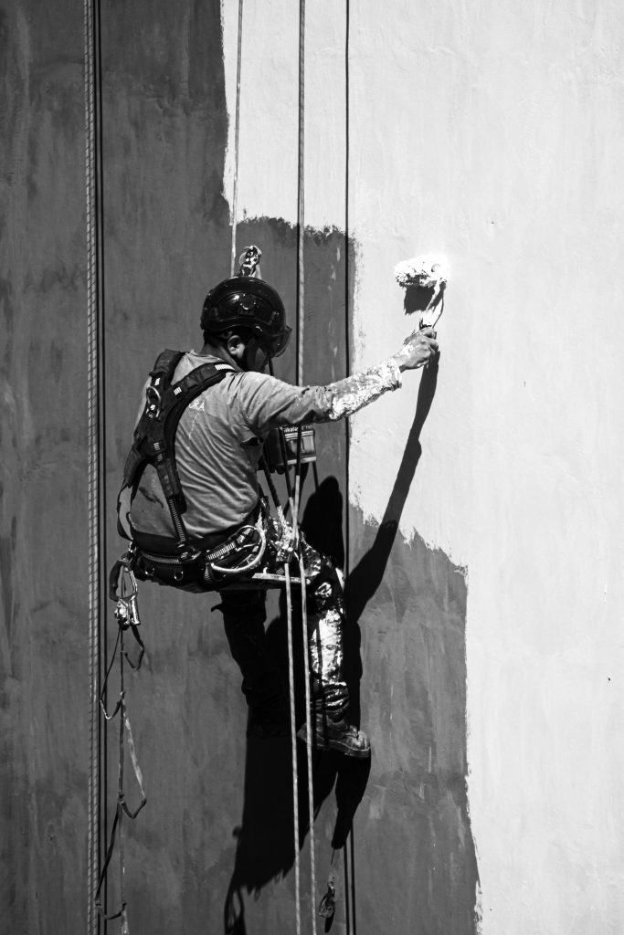 A worker uses rope access to paint a building wall in Buenos Aires, highlighting industrial labor practices.