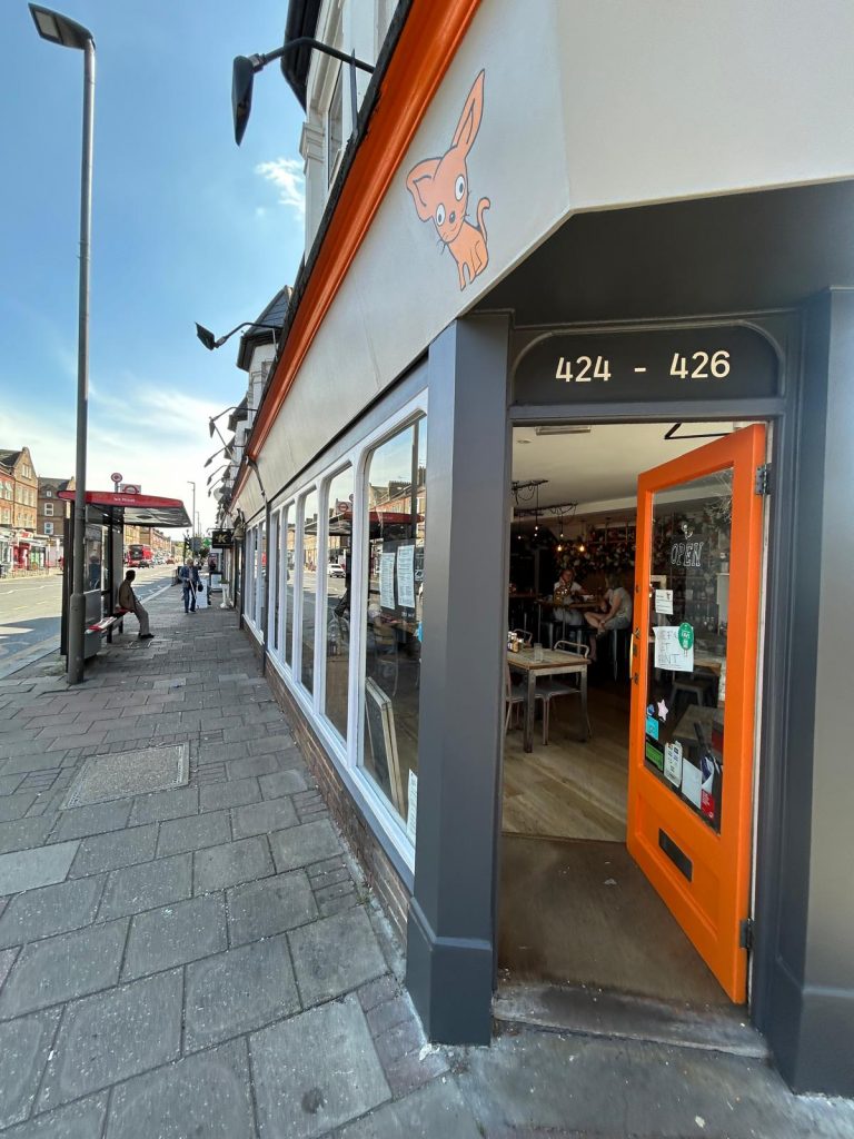 Completed shopfront restoration for a Wimbledon boutique cafe featuring a signature orange door and charcoal grey façade.